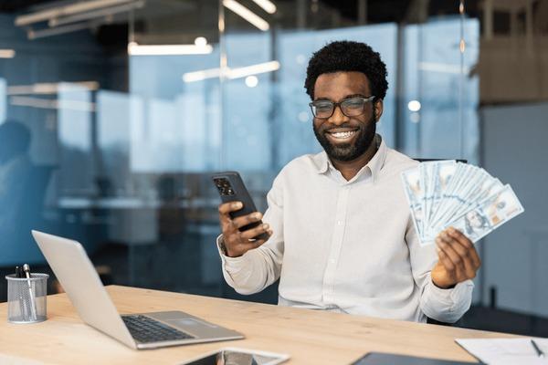 Smiling man holding cash and smartphone